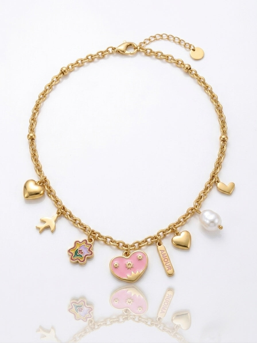 A gold-tone charm necklace featuring multiple heart and flower charms, including a pink heart with a pearl center, a flower with green and blue accents, and a white pearl bead, displayed on a clean white background with a soft reflection.