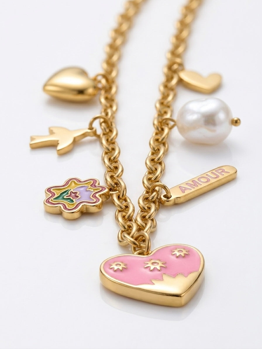 Gold-tone charm necklace featuring a pink heart pendant, a pearl bead, a bird charm, a flower charm, and a bar charm engraved with 'AMOUR' on a white background.