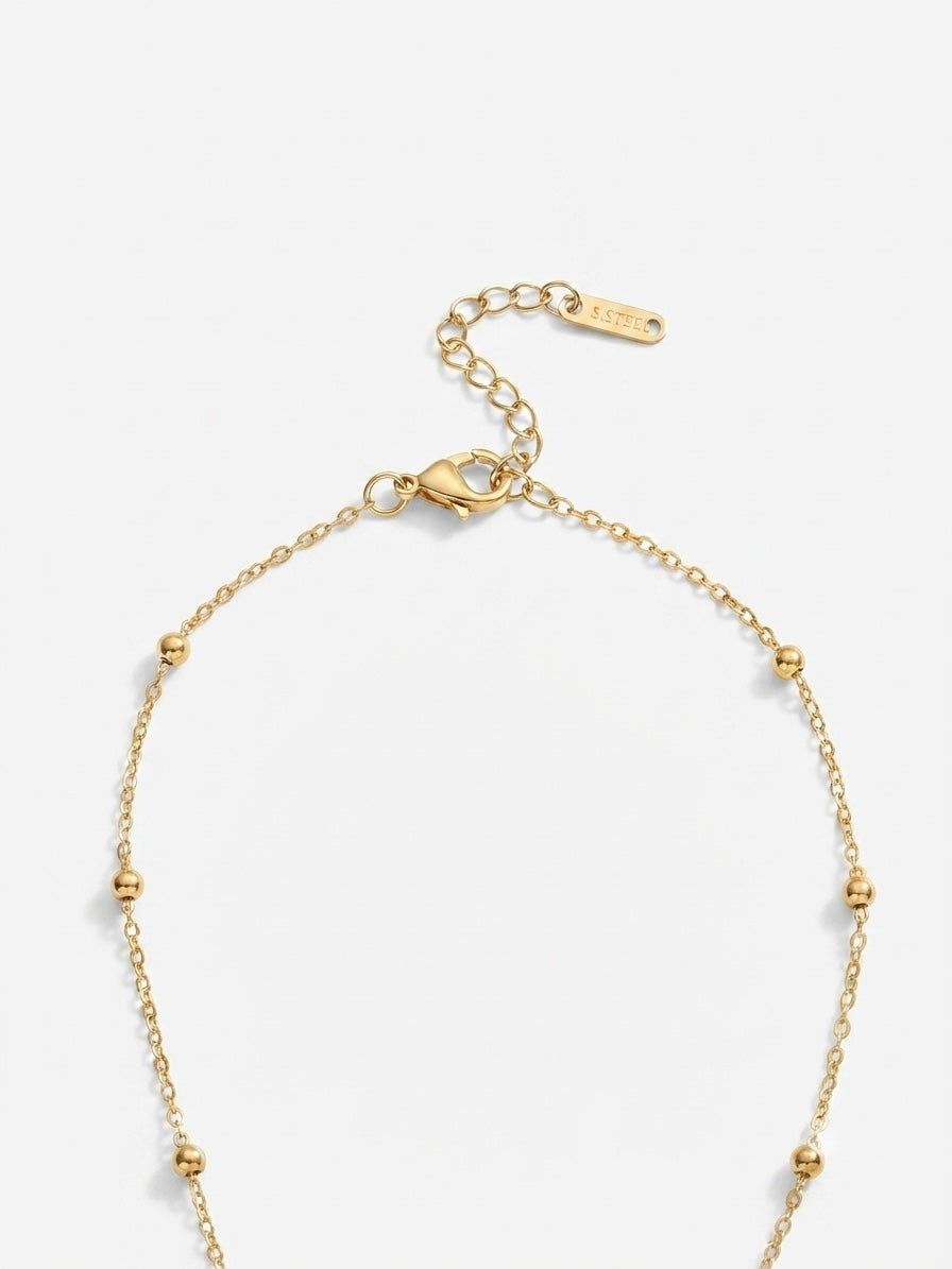 A delicate gold chain necklace with small bead accents, a lobster clasp, and an adjustable extension chain, shown on a light gray background.
