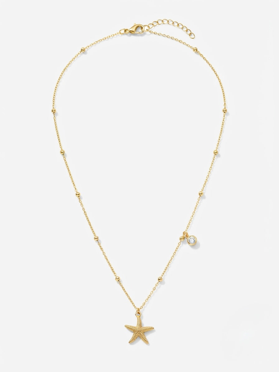 A delicate gold chain necklace featuring a small starfish pendant at the center, accented with tiny bead details and a small clear stone charm, displayed on a light gray background.