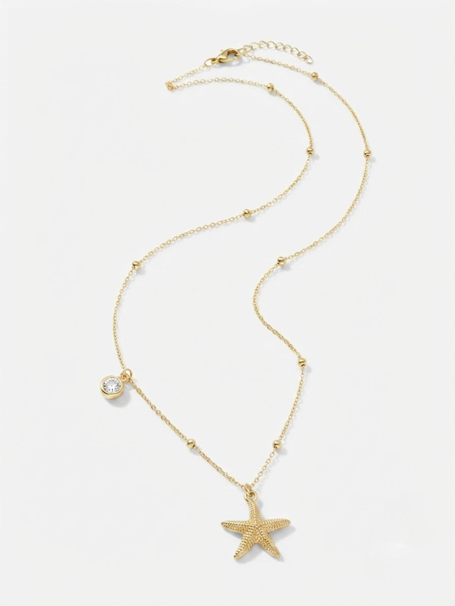 A delicate gold chain necklace featuring a textured starfish pendant, small bead accents, and a bezel-set clear crystal charm, displayed on a clean white background.